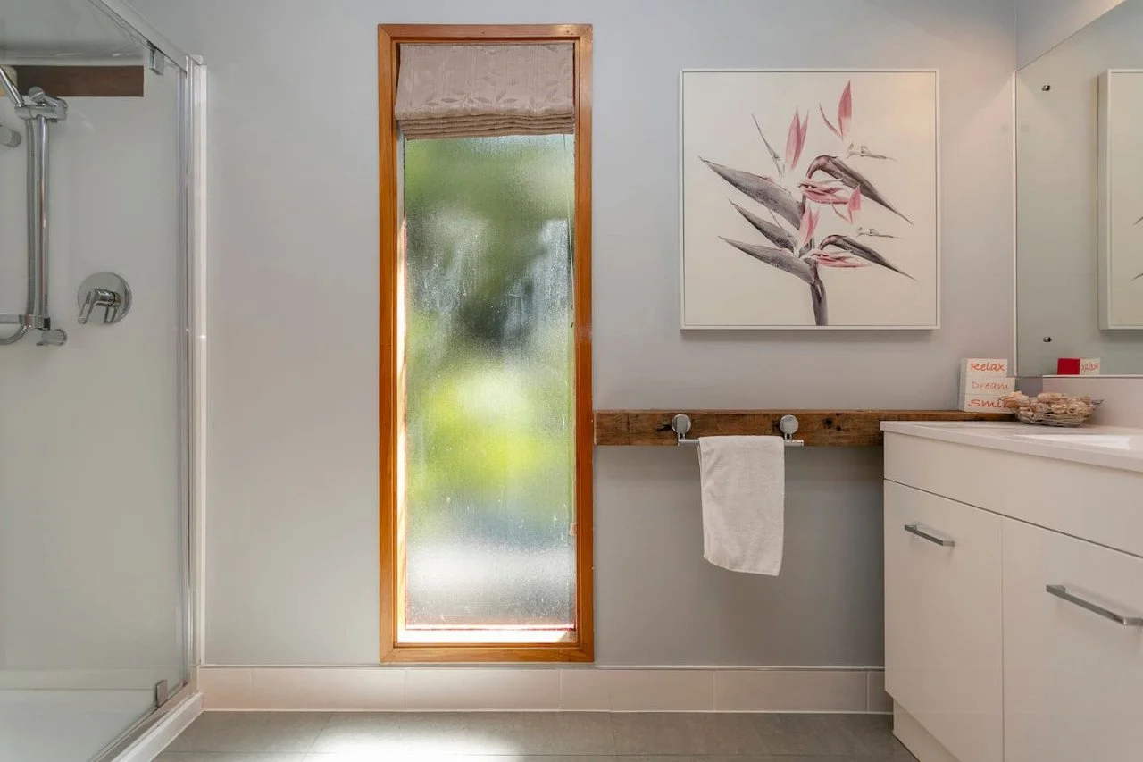 Modern bathroom with frosted window, white sink, and artwork of bird of paradise on the wall.