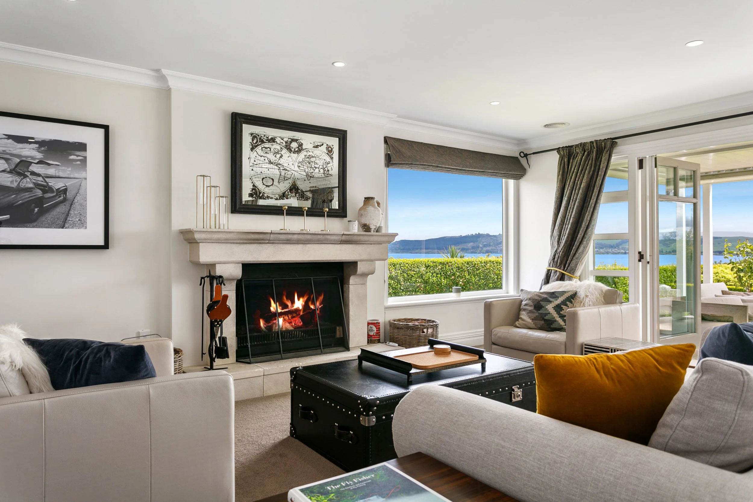 Living room with a fireplace, large window showing a view of water and hills, and seating area with cushions.