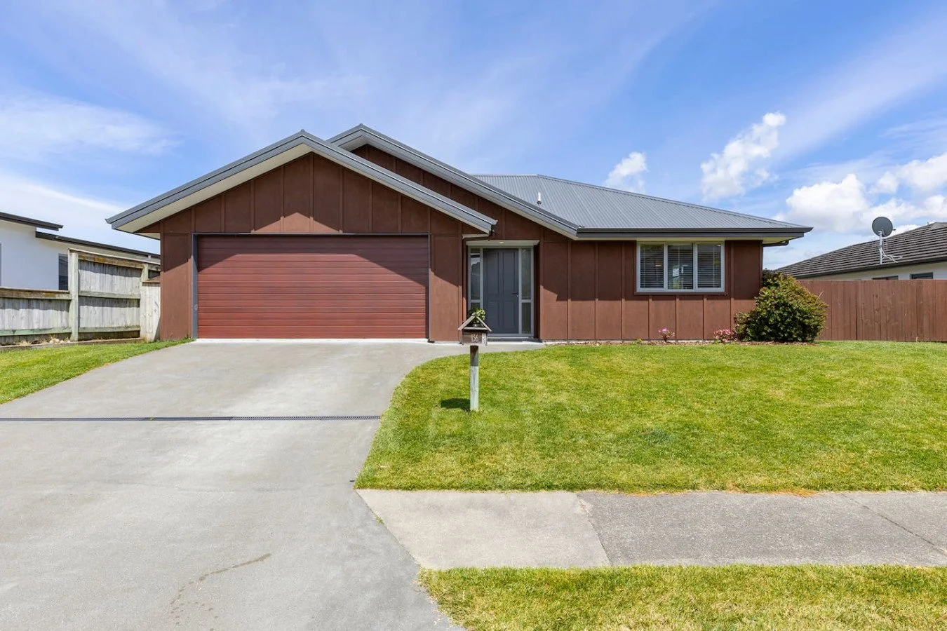 Front view of a single-story house with a two-car garage, brown exterior, and a small front yard with green grass and a mailbox.