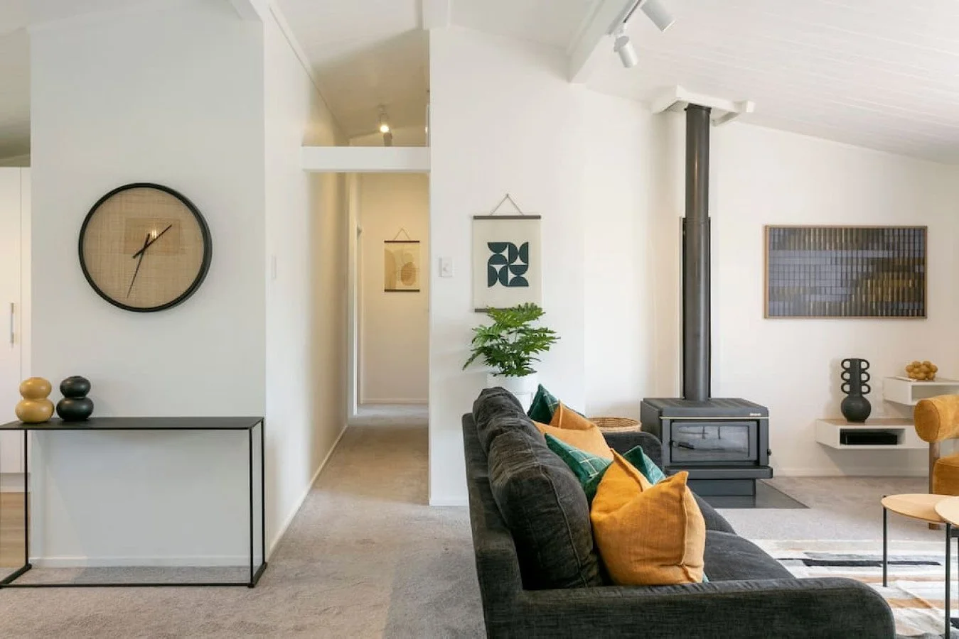Living room with black couch, colorful pillows, a wood stove, and modern decor in a bright, minimalistic style.