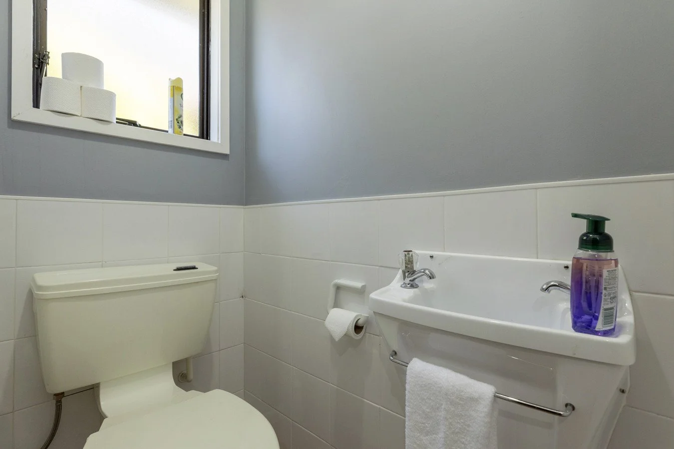 Bathroom with toilet, small sink with soap dispenser, and window with toiletries.
