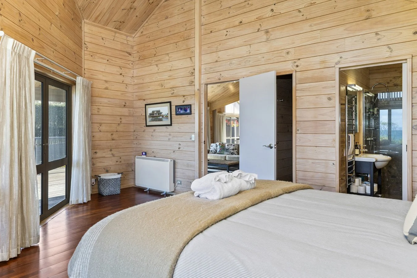 Bedroom with wood-paneled walls, a large bed with beige bedding, and a towel folded into a swan shape, with open doorway leading to a bathroom.