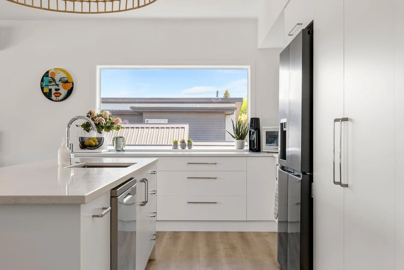 Modern white kitchen with a large window, stainless steel appliances, and minimal decor.