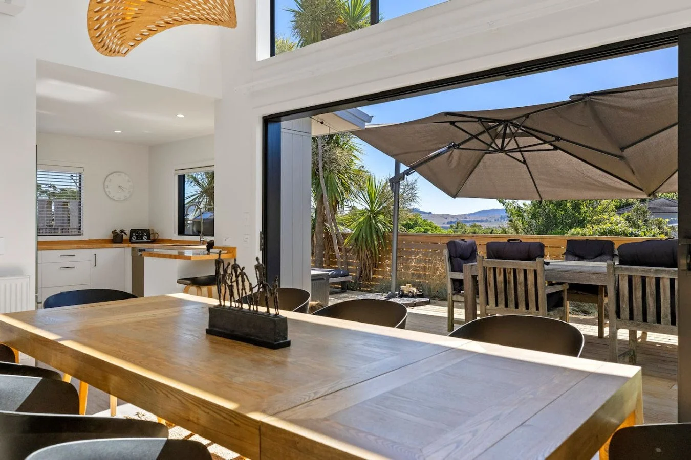 Open-plan kitchen and dining area with large sliding glass door leading to outdoor patio with table, chairs, umbrella, and greenery.