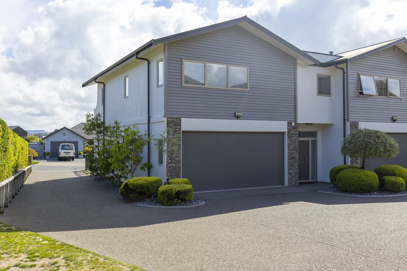 Modern two-story suburban house with gray siding, a garage, and landscaped yard with trimmed bushes and small trees