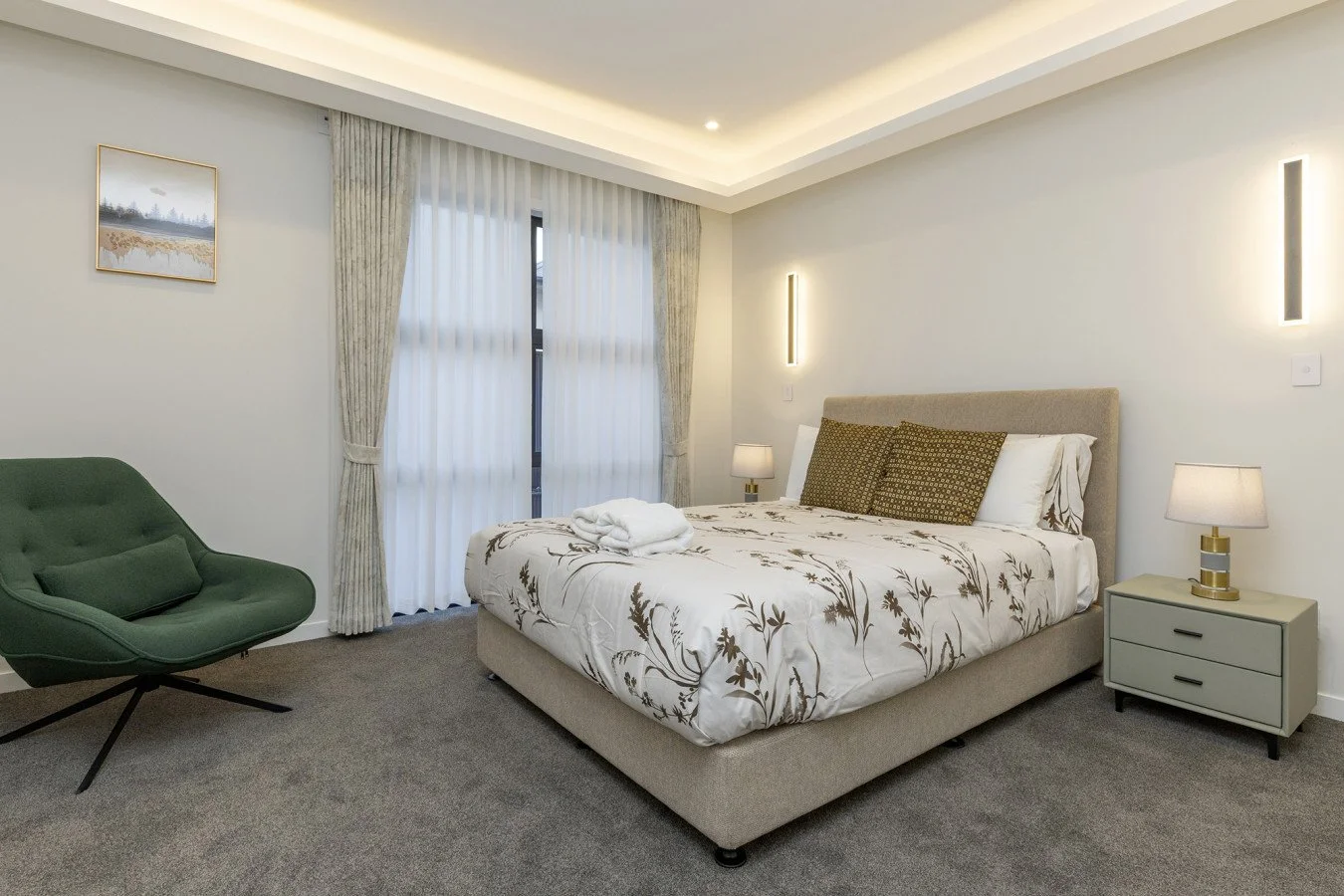Modern bedroom with a bed, green armchair, framed art on wall, and a large window with curtains.