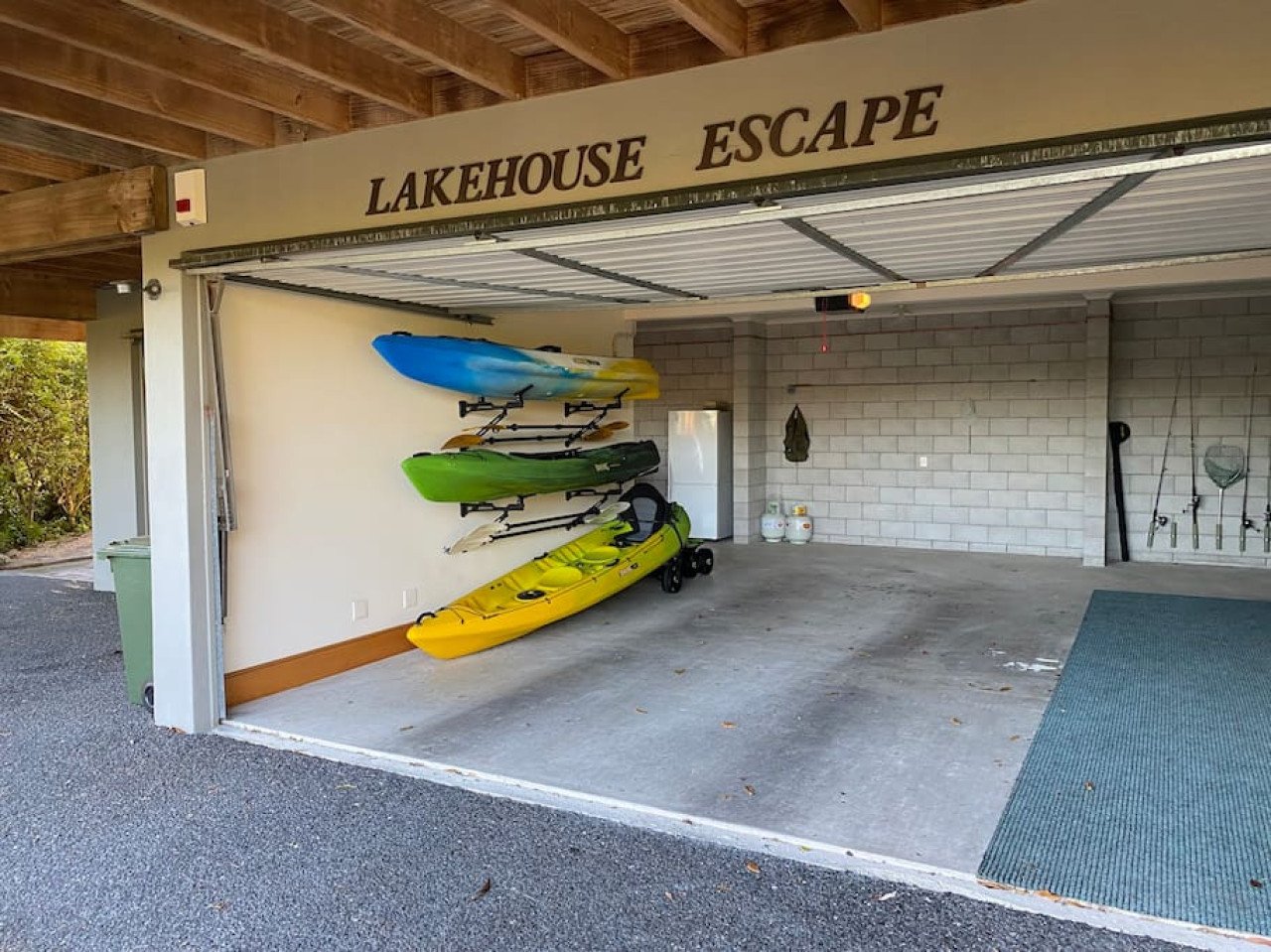 Garage with kayaks and paddles stored on wall, propane tanks on floor, and fishing gear hanging on wall, with a sign that reads "Lakehouse Escape."