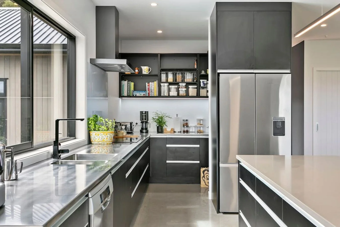 Modern kitchen with black cabinets, stainless steel appliances, a large refrigerator, a kitchen island, and a window with a view outside.