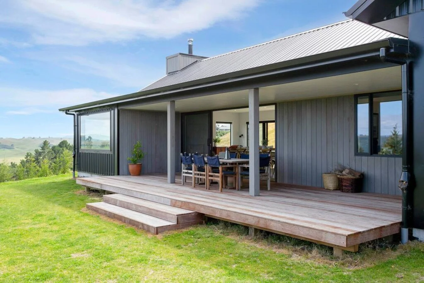 A modern house with a wooden deck overlooking a green landscape under a partly cloudy sky.