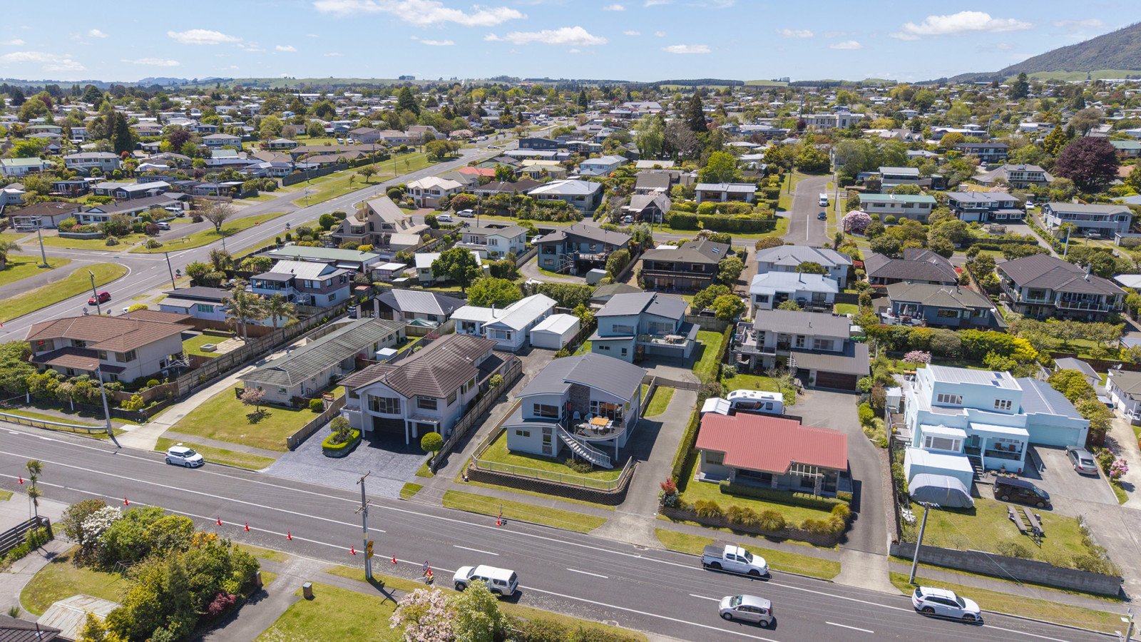 Aerial view of a suburban neighborhood with houses, streets, trees, and cars on a sunny day.