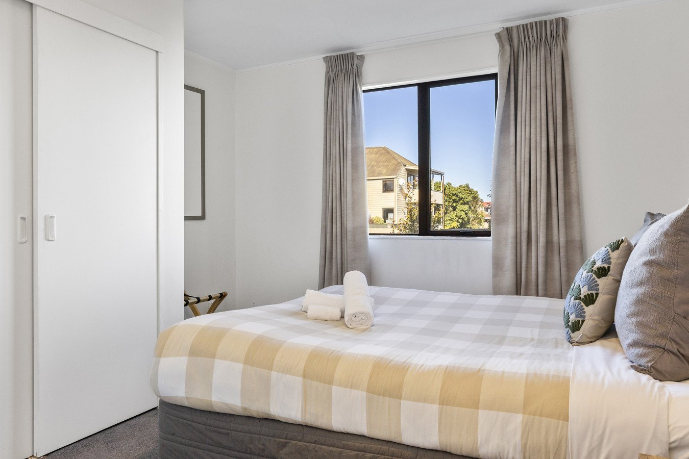 A simple hotel bedroom with a bed, window, beige curtains, and white walls.