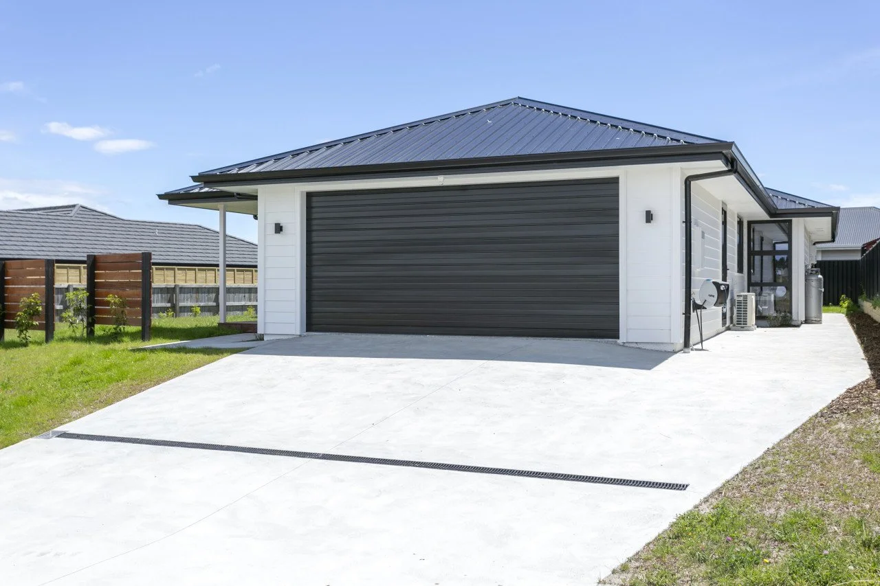 Modern house with a concrete driveway, black garage door, and white siding, located in a suburban neighborhood.