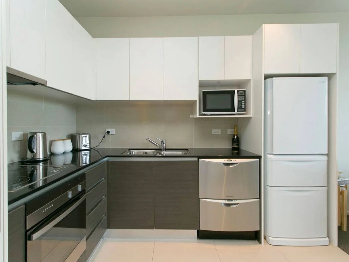 Modern kitchen with white upper cabinets, dark lower cabinets, a stainless steel oven, microwave, fridge, sink, and various small appliances.