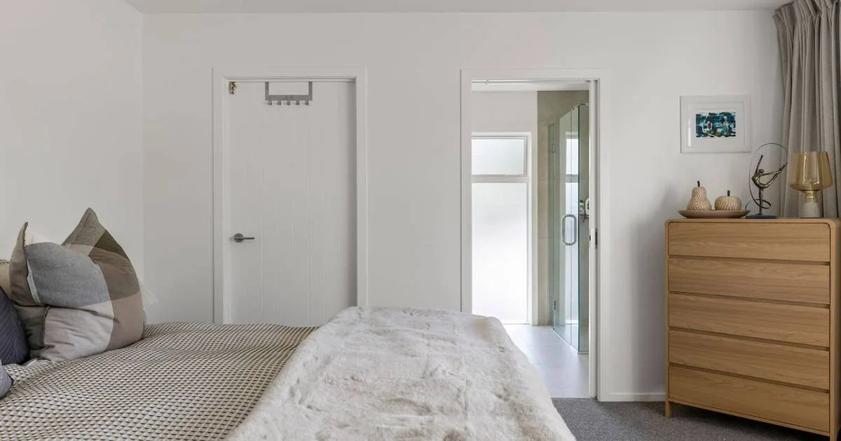 A bedroom with a bed, nightstand, and a door leading to a bathroom with a shower and glass door.