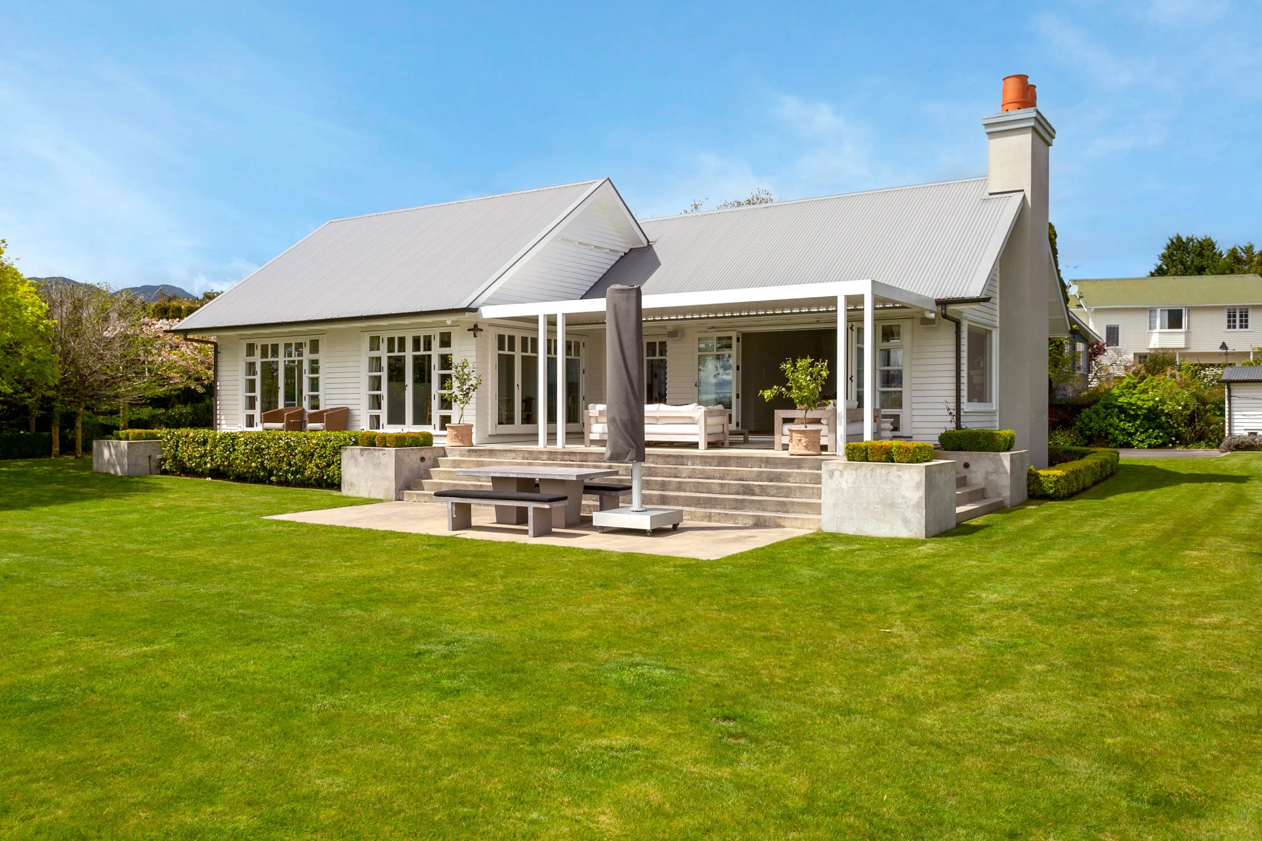White house with a gabled metal roof, large front porch, and green lawn, under a blue sky.