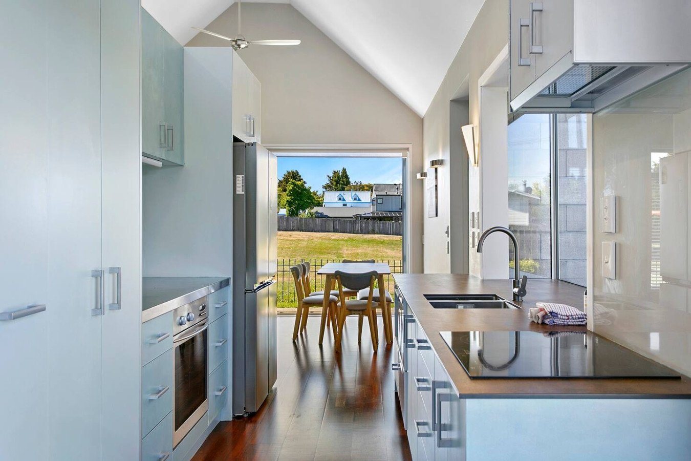 Modern kitchen with white cabinets, a black stove, and a double sink, with a view of the backyard and patio area with chairs through a large open door.