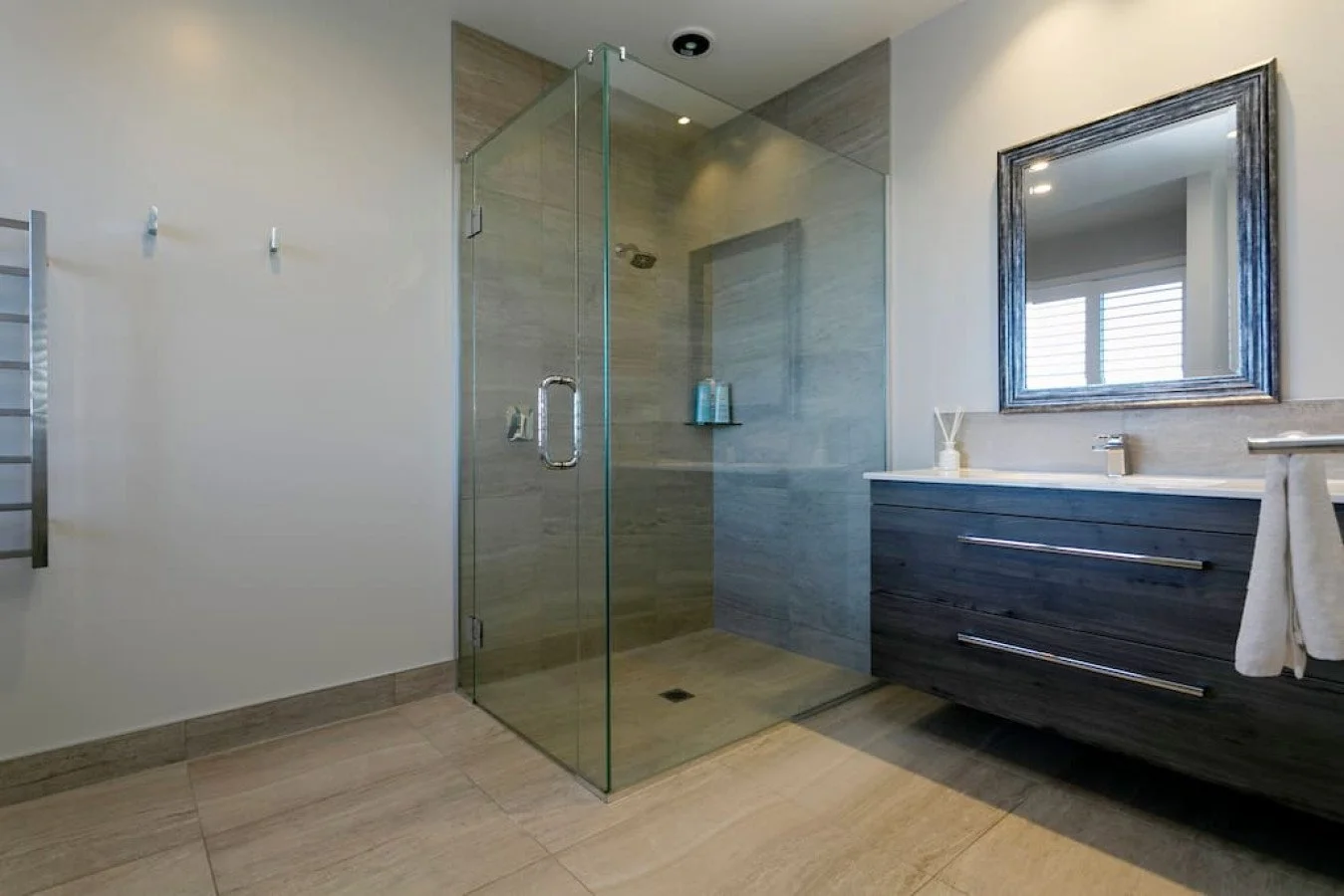 Modern bathroom with a glass shower enclosure, a dark wood vanity with a white countertop, a large mirror, and a window with blinds.