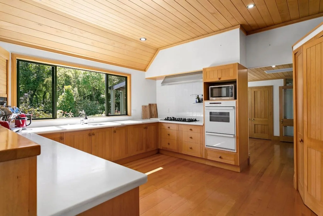 Kitchen with wooden cabinets, white countertops, a large window overlooking greenery, and built-in appliances including an oven and microwave.