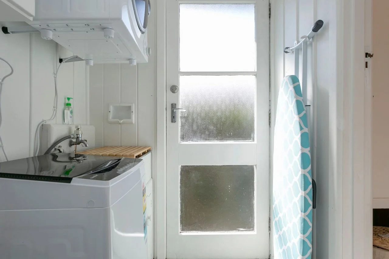 Small laundry room with a washing machine, ironing board, and an outdoor door with frosted glass panels.