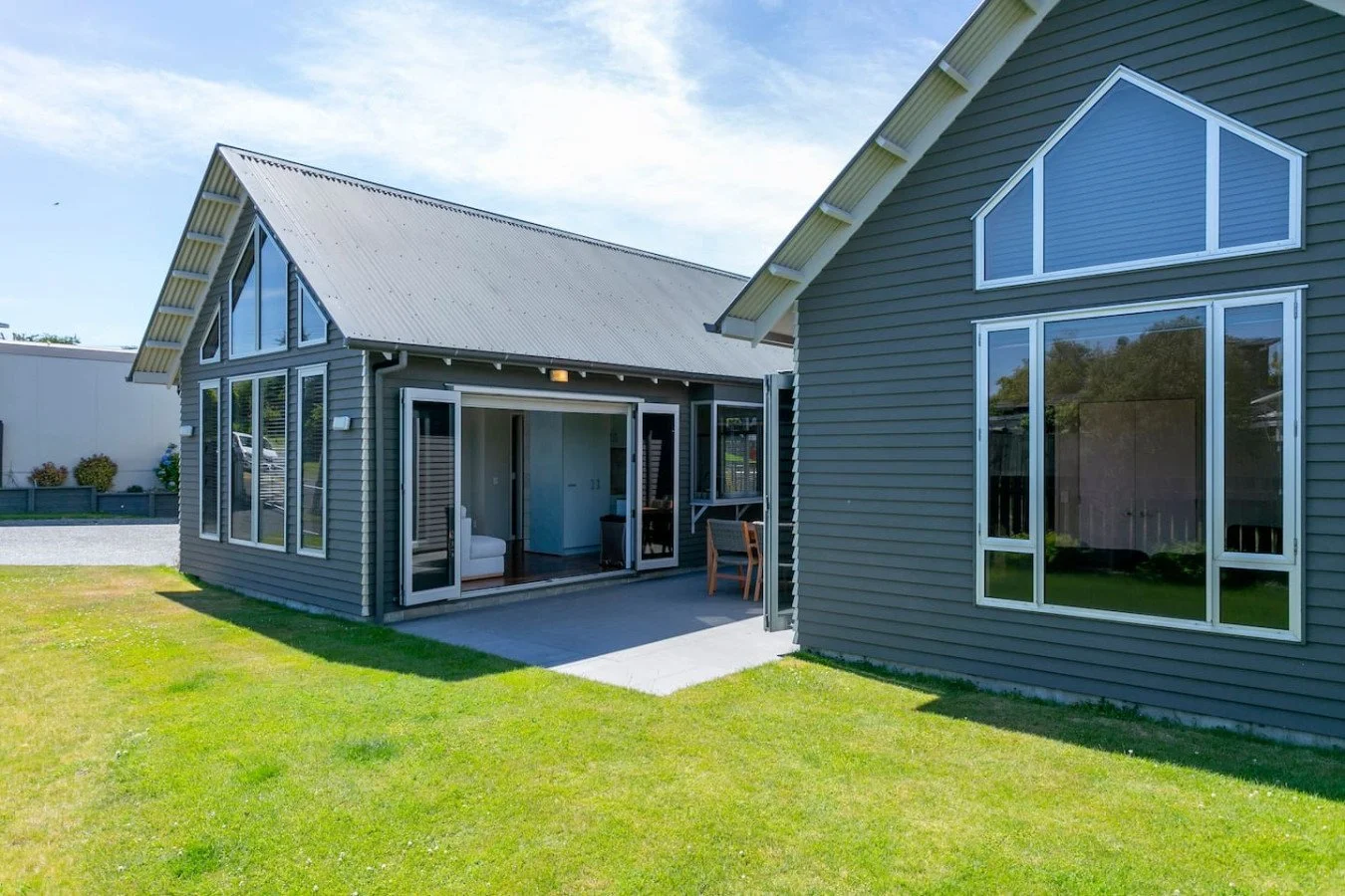 A modern house with gray siding and large windows, with a well-kept lawn and a wooden deck in a suburban neighborhood.