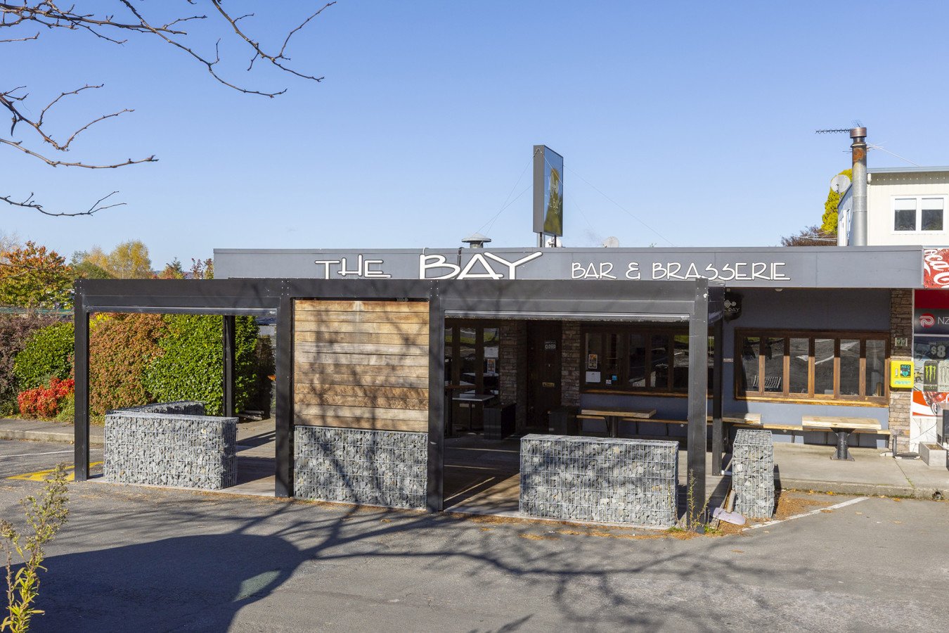 Exterior of a bar and brasserie named 'The Bay' with outdoor seating area and greenery in the background.