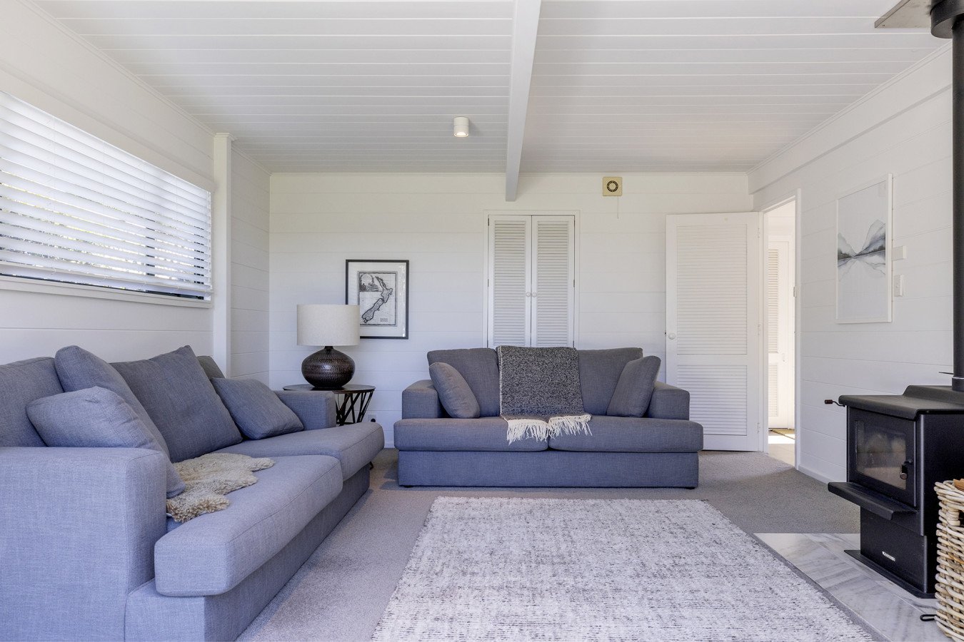 Living room with two gray sofas, a side table with a lamp, wall art, a rug, and a wood stove in the corner.