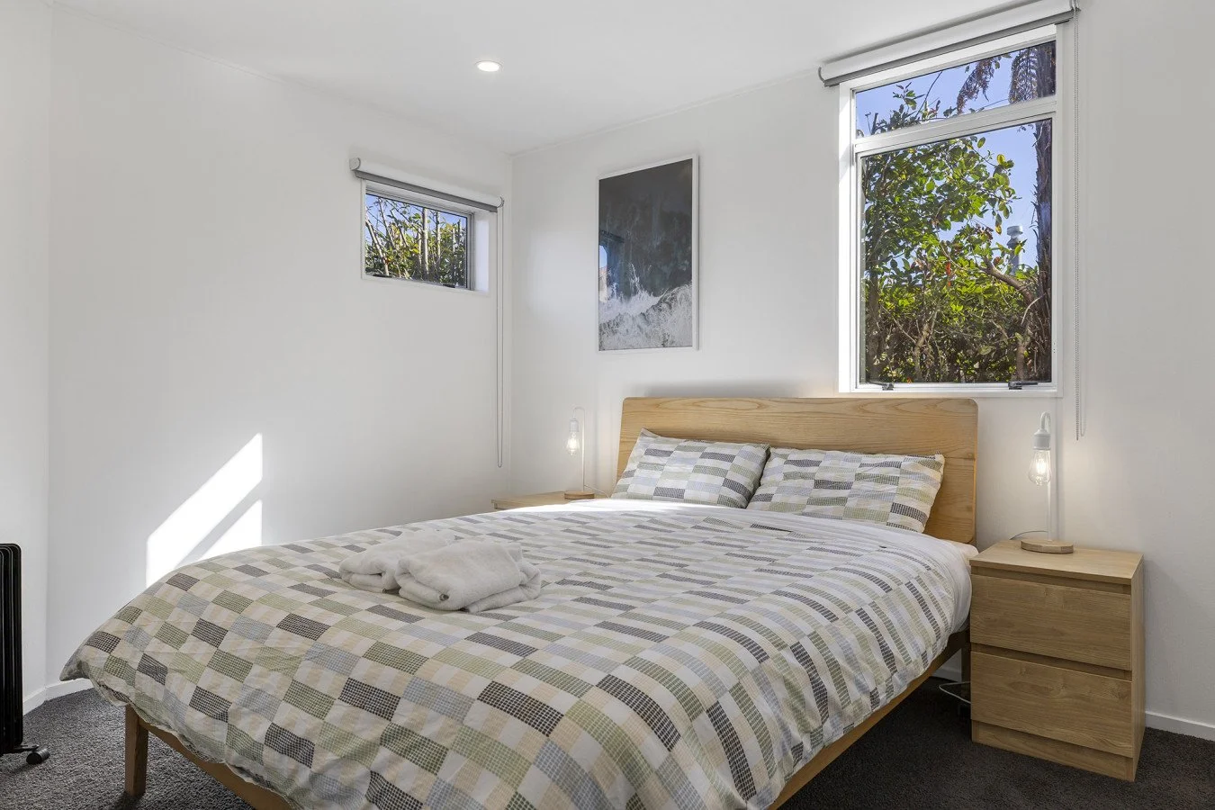 Bedroom with a bed, two pillows, a wooden headboard, two small side tables with lamps, a window, and modern art on the wall.
