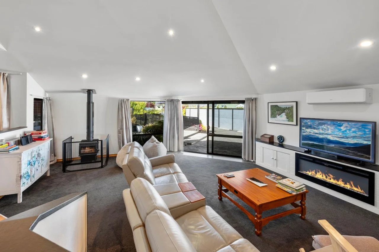 Living room with beige leather sofas, a wooden coffee table, a flat-screen TV, a modern fireplace, and a sliding glass door leading to an outdoor patio.
