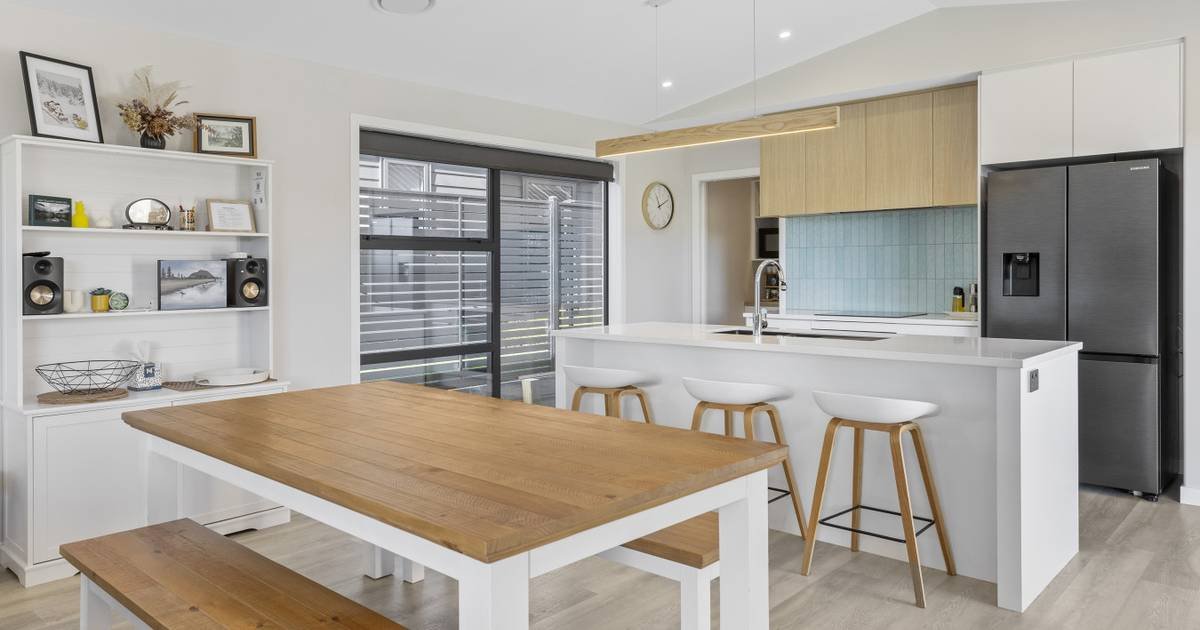 Modern kitchen with white and wooden cabinetry, stainless steel refrigerator, bar stools at a breakfast bar, and a dining table.