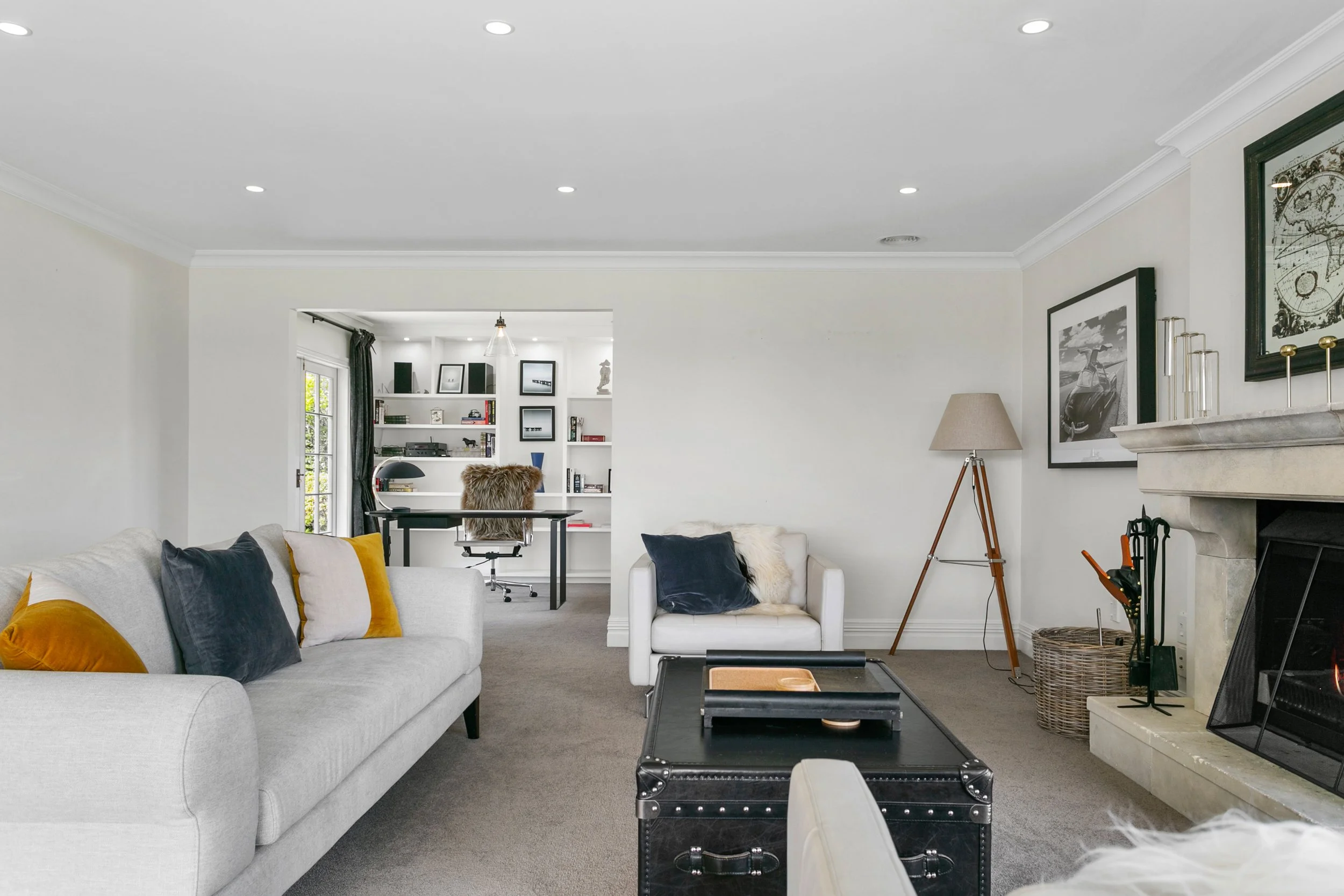 Living room with gray sofa, white armchair, fireplace, framed black and white artwork, and a bookcase in the background