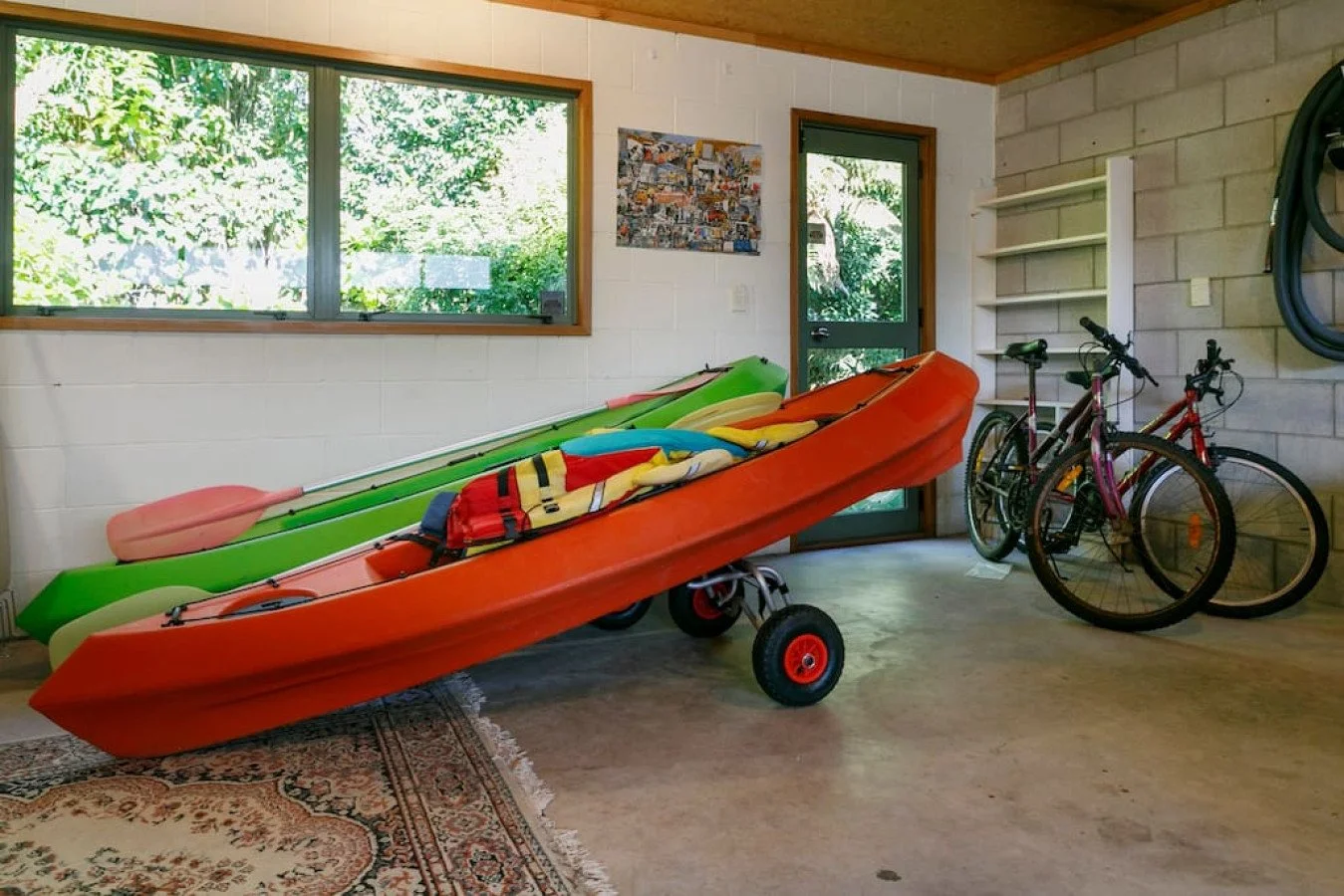 Garage with orange and green kayaks, two bicycles, and shelves on the wall.