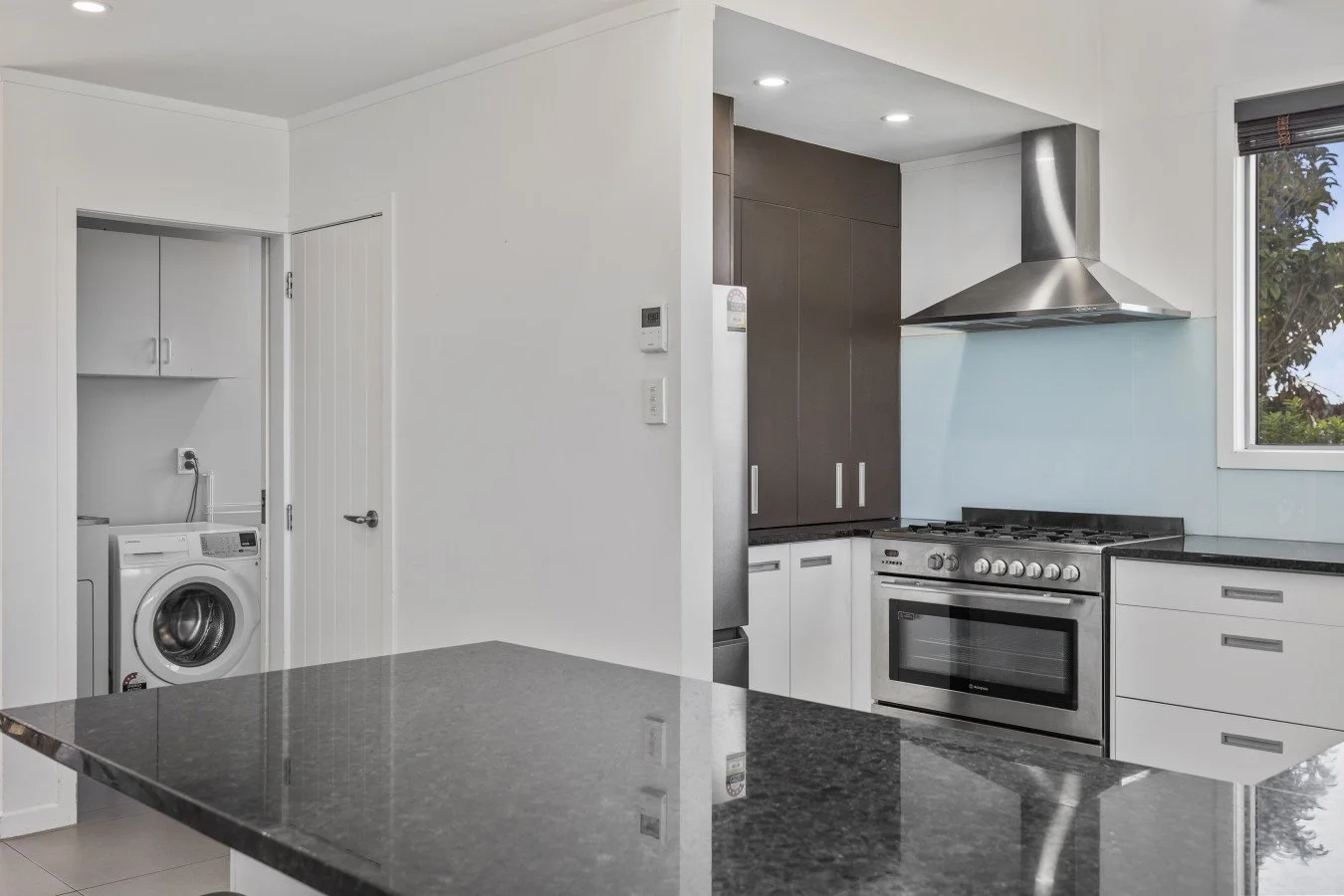 Modern kitchen with black granite island, stainless steel appliances, dark brown and white cabinets, and a laundry area with a washing machine.