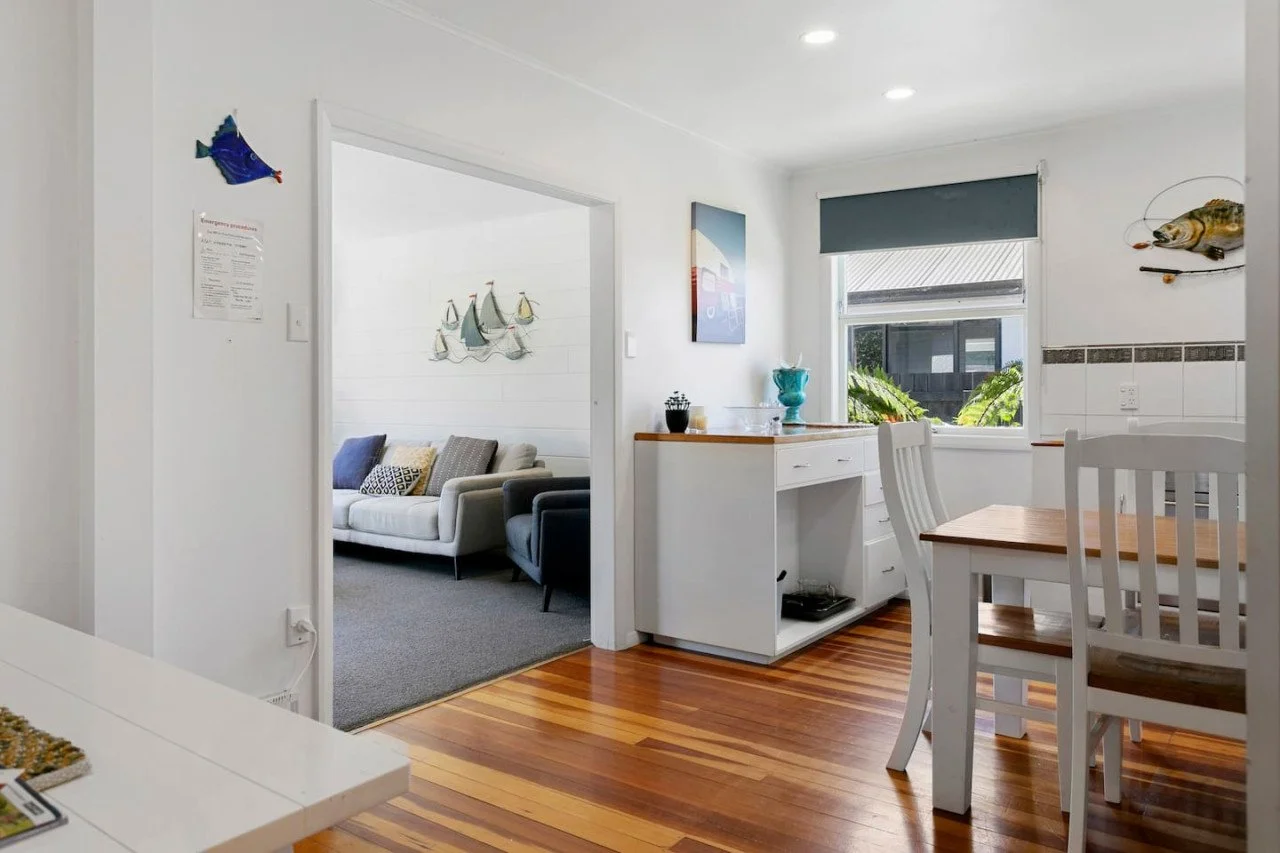 View of a dining area and living room with white walls and wooden floors, decorated with fish-themed wall art and bright decor.