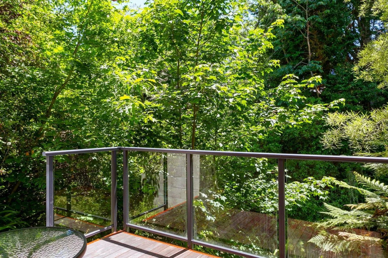 A balcony with a glass and metal railing overlooking a lush green forest with various trees and foliage.