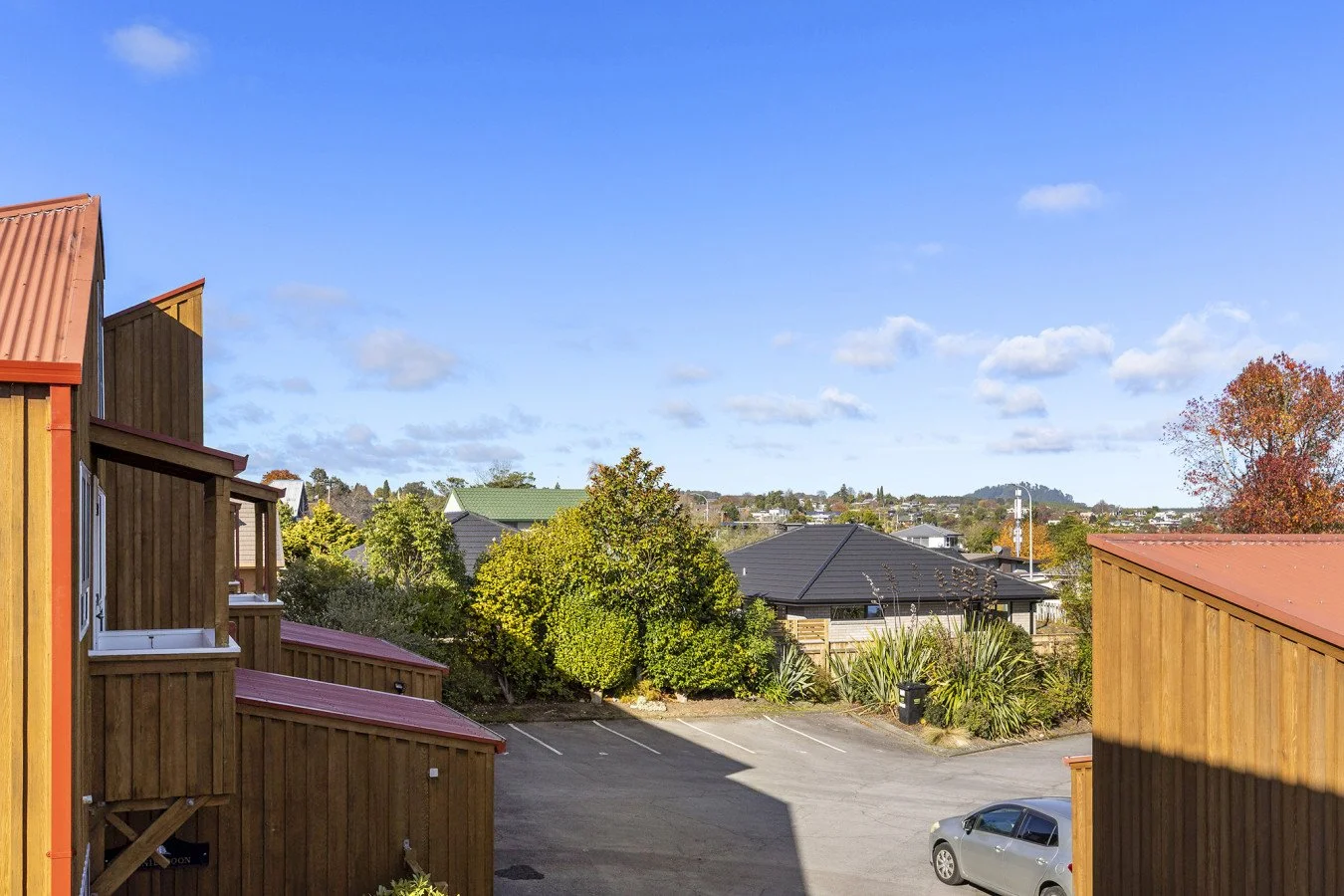 View of a parking lot with trees and houses in the background under a partly cloudy blue sky.