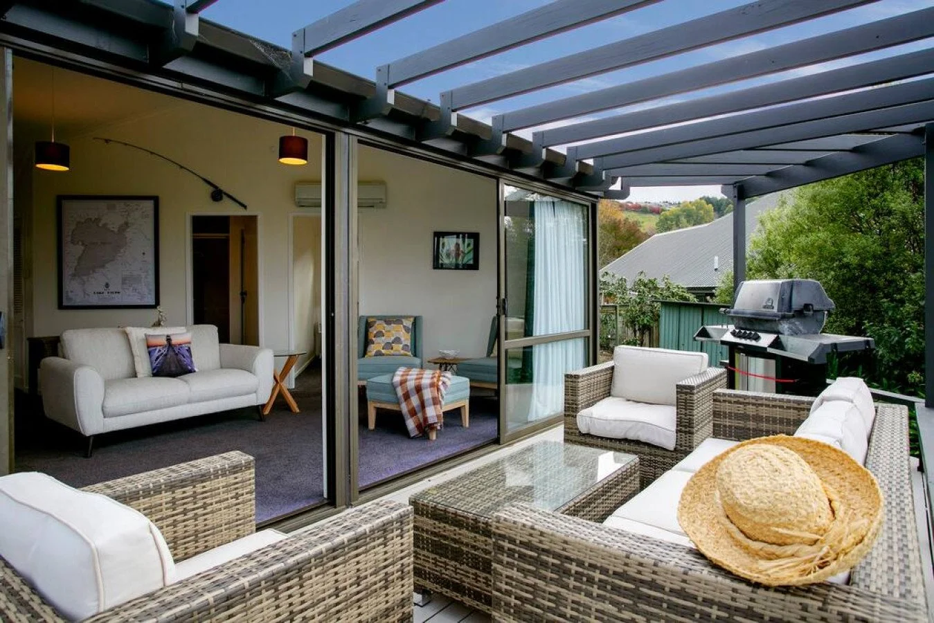 Outdoor patio with wicker furniture, white cushions, a grill, and a view of trees and rooftops.