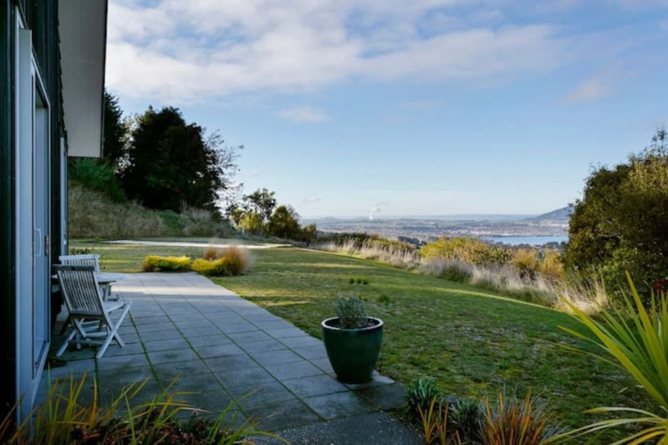 View of a backyard with a patio, potted plants, and a scenic landscape with trees, water, and hills in the distance.
