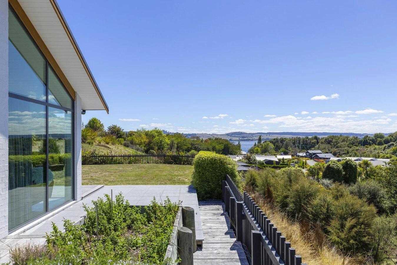 View from a house patio overlooking a lush green landscape with trees, a body of water, and a clear blue sky with some clouds.