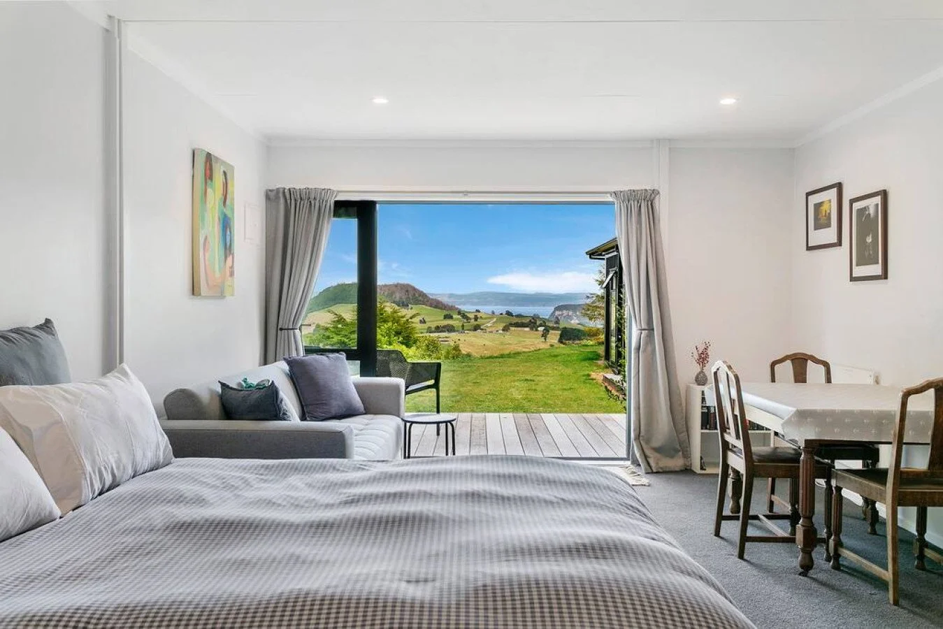 Living room with a large window showing a scenic outdoor landscape including fields, trees, hills, and water in the distance.