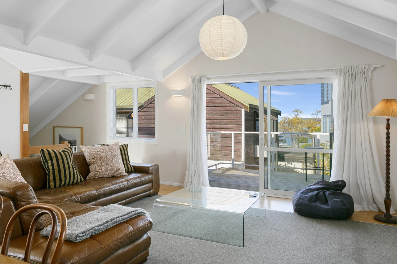 Living room with a brown leather sofa, pillows, a glass coffee table, window and sliding door leading to a balcony, and a floor lamp.