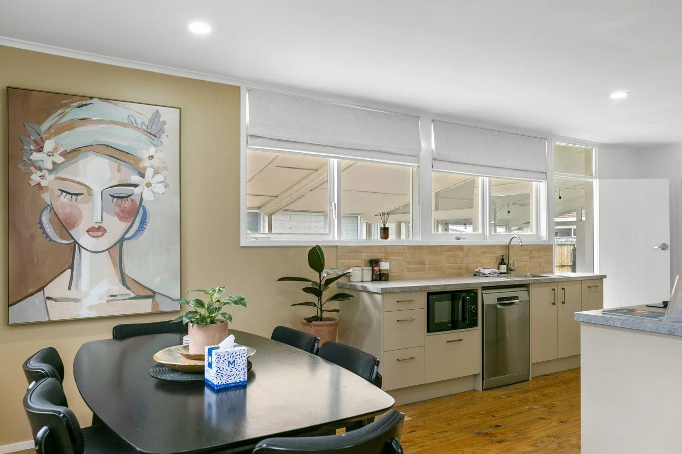Kitchen with a dining table, plants, artwork, and windows.