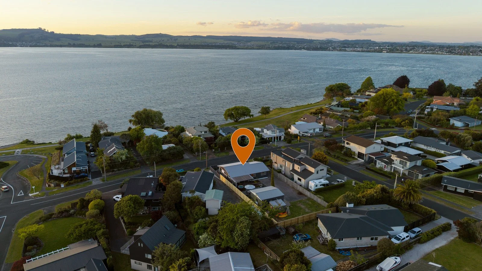 Aerial view of a neighborhood near a body of water, with houses, trees, and roads, and a marker indicating a specific house.