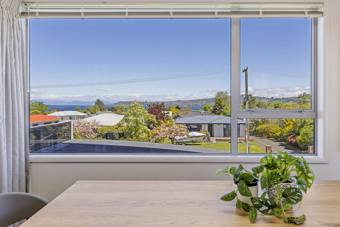 View of a residential neighborhood with trees, houses, and a mountain range in the distance through a large window from inside a room.