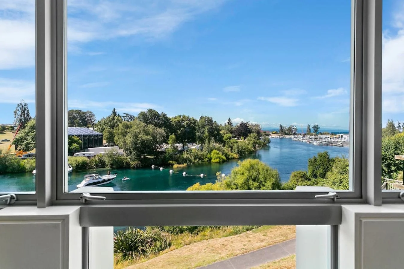 Scenic view of a river with boats and lush green trees through a large open window during the day.