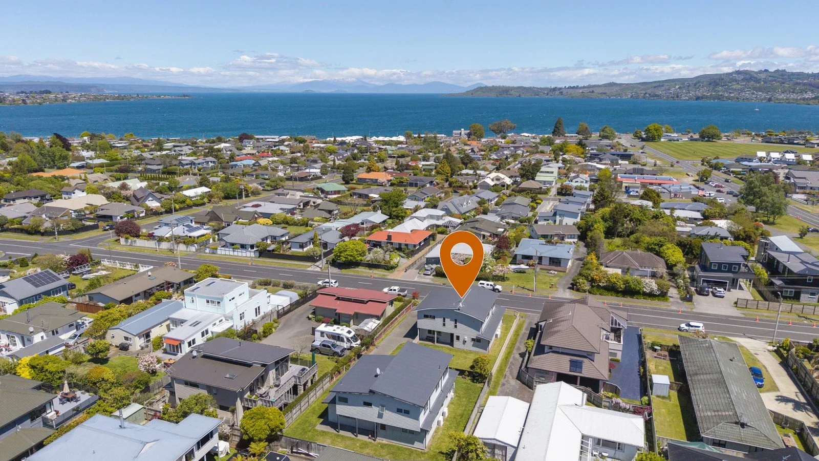 Aerial view of a residential neighborhood by a large body of water with mountains in the distance, with a house marked by an orange location pin.