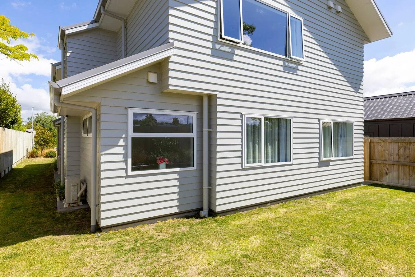 A two-story house with white siding, multiple windows with curtains, and a backyard with a grassy lawn.