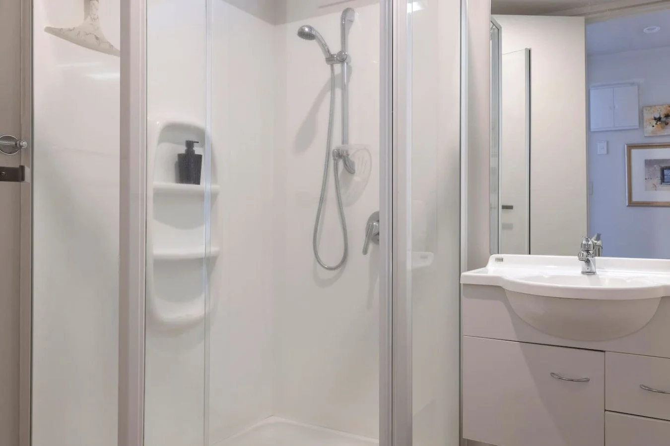 A clean, modern bathroom with a glass-enclosed shower on the left and a white vanity with a mirror on the right.