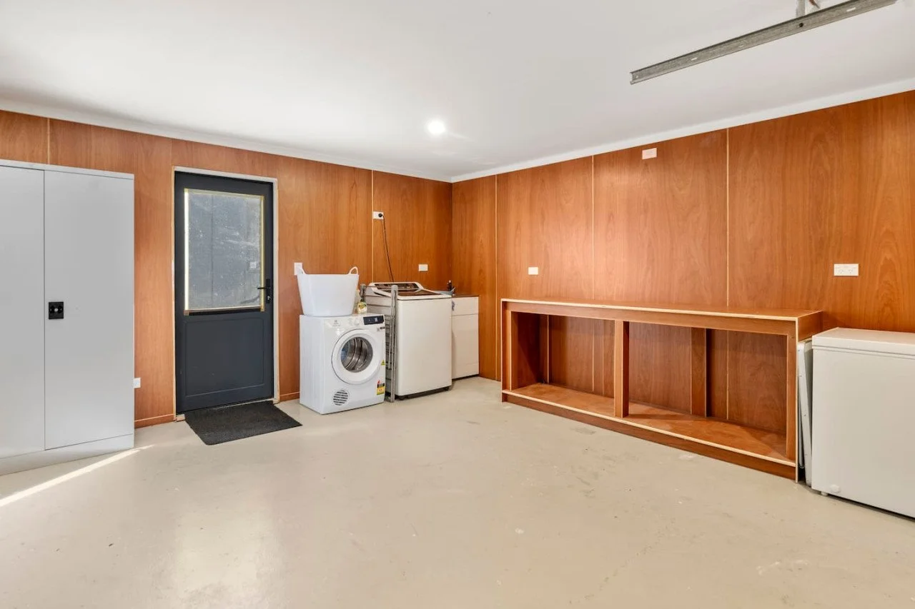 Laundry room with washing machine, dryer, storage cabinets, and utility sink, all against wooden-paneled walls.