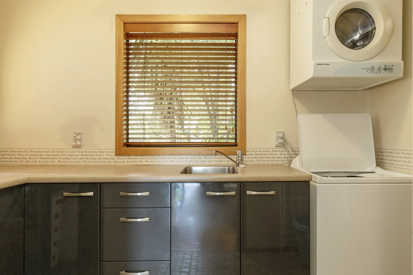 Kitchen with a window behind a sink, a washer and dryer stacked on the right, and dark cabinetry below the countertop.