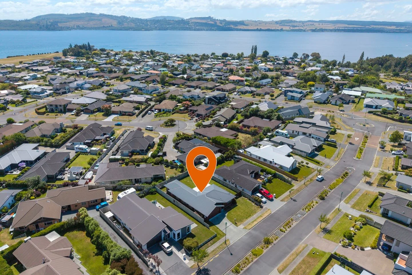 Aerial view of a residential neighborhood near a large body of water, with a mix of houses and streets, and an orange location marker on one house.